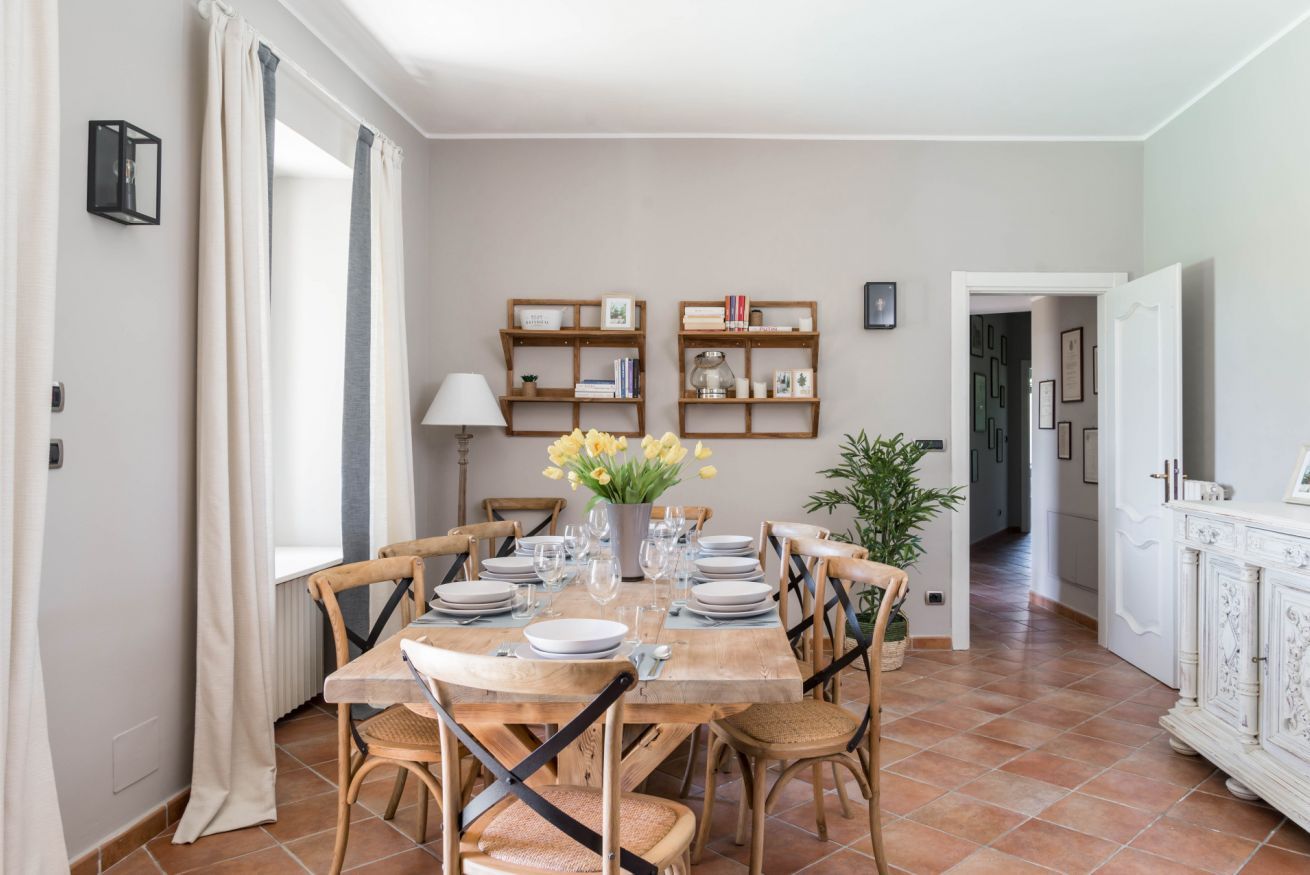 A dining area with a wooden table set for four, surrounded by chairs, with a vase of flowers on the table.