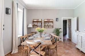 Un coin repas avec une table en bois dressée pour quatre personnes, entourée de chaises, et un vase de fleurs posé sur la table.