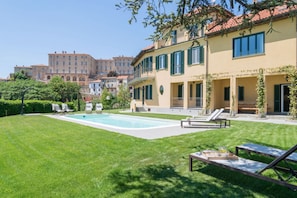 Une piscine avec des chaises longues, une pelouse bien entretenue et un bâtiment doté de balcons.