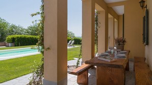 Un espace extérieur abrité où l’on peut prendre ses repas, avec une piscine en arrière-plan.