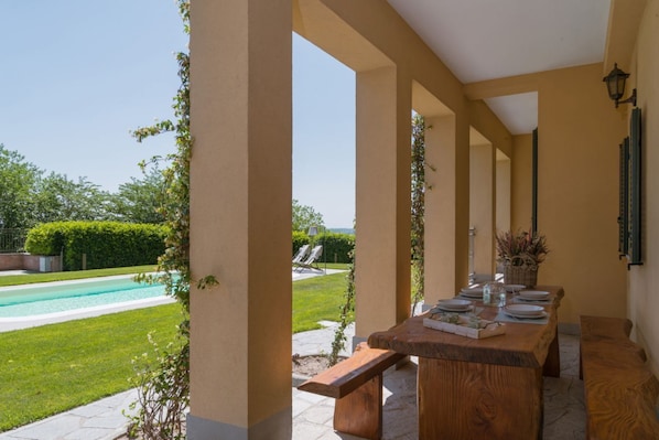 A covered outdoor dining area with a pool in the background.