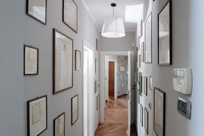Un couloir orné de documents encadrés aux murs, un luminaire suspendu blanc et une porte donnant sur une autre pièce.