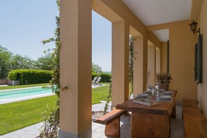 Un espace extérieur abrité où l’on peut prendre ses repas, avec une piscine en arrière-plan.