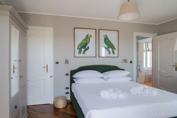 Une chambre à coucher avec un lit, du linge de lit blanc, deux tableaux représentant des oiseaux, une lampe de chevet et une porte avec un miroir.