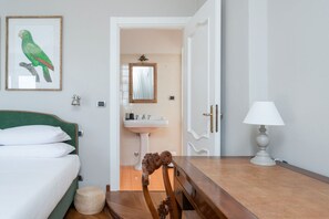 A bedroom with a bed, a wooden dresser, a lamp, a framed picture of a parrot, and a bathroom with a sink and mirror. - GuestHost - Elegant and spacious villa perfect for accommodating up to 12 guests is located in the center of Vignale in the heart of Monferrato area, nominated a UNESCO World Heritage Site in 2014. The house is equipped with every comfort: WiFi, air cond (Vignale Monferrato)