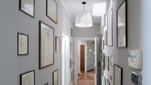 Un couloir orné de documents encadrés aux murs, un luminaire suspendu blanc et une porte donnant sur une autre pièce.