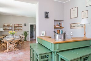 Un comedor con mesa y sillas de madera, un banco verde, y una cocina con pileta y encimera.