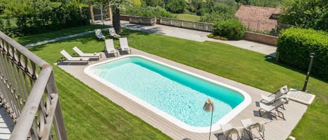 A rectangular swimming pool with a wooden deck, surrounded by a well-maintained lawn and a wooden fence.