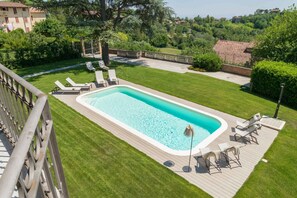 Una piscina rectangular con una cubierta de madera, rodeada por un césped cuidado y una valla de madera.