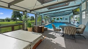 A covered outdoor area with a pool, seating, and a view of a green landscape. - Indoor Pool & Hot Tub on Golf Course (Loveland)