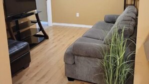 Una sala de estar con televisión de pantalla plana, un sofá gris, un cuadro en la pared y una planta en maceta.