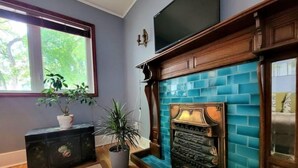 Una habitación con chimenea, televisión y ventana con vistas a zonas verdes.