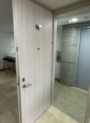 Ein modernes Zimmer mit einer Holztür, einem kleinen Schreibtisch mit Stuhl und einer strukturierten Wand.