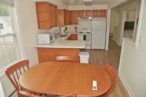 Kitchen area with a central island, microwave, stove, and refrigerator. Dining table and chairs nearby.