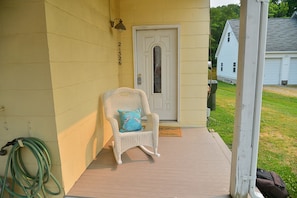 A porch with a wicker rocking chair and a door.