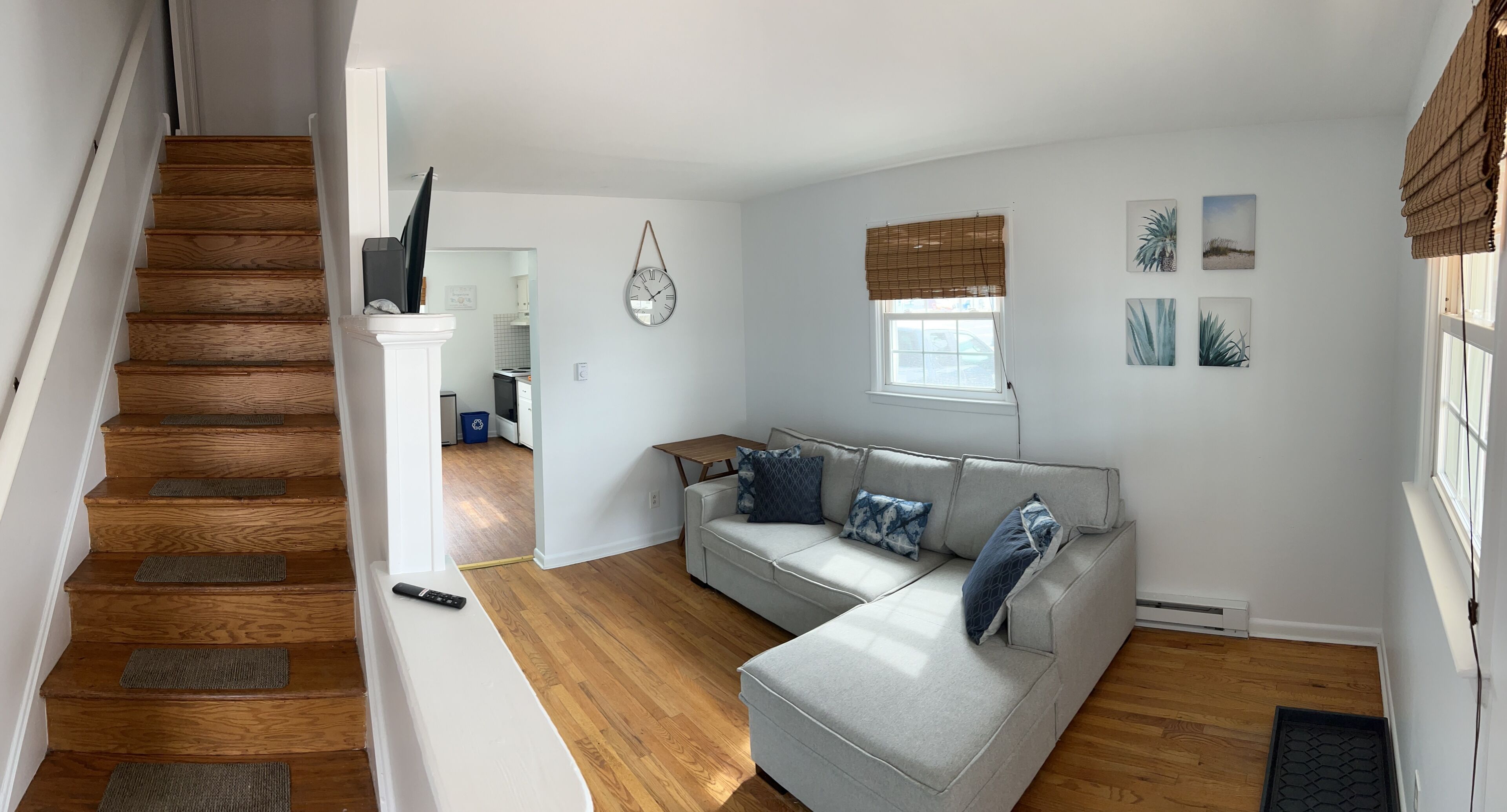 Sala de estar com sofá modular cinza, escadas de madeira e uma cozinha ao fundo.