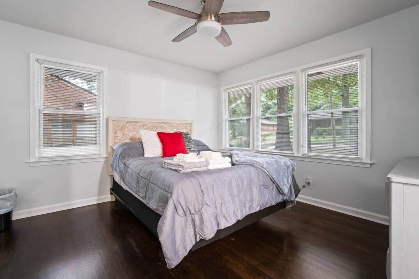 Un dormitorio con cama, ventilador de techo y ventanas grandes.