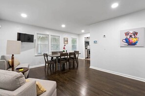 Una sala de estar moderna con comedor, pisos de madera y una cocina al fondo.
