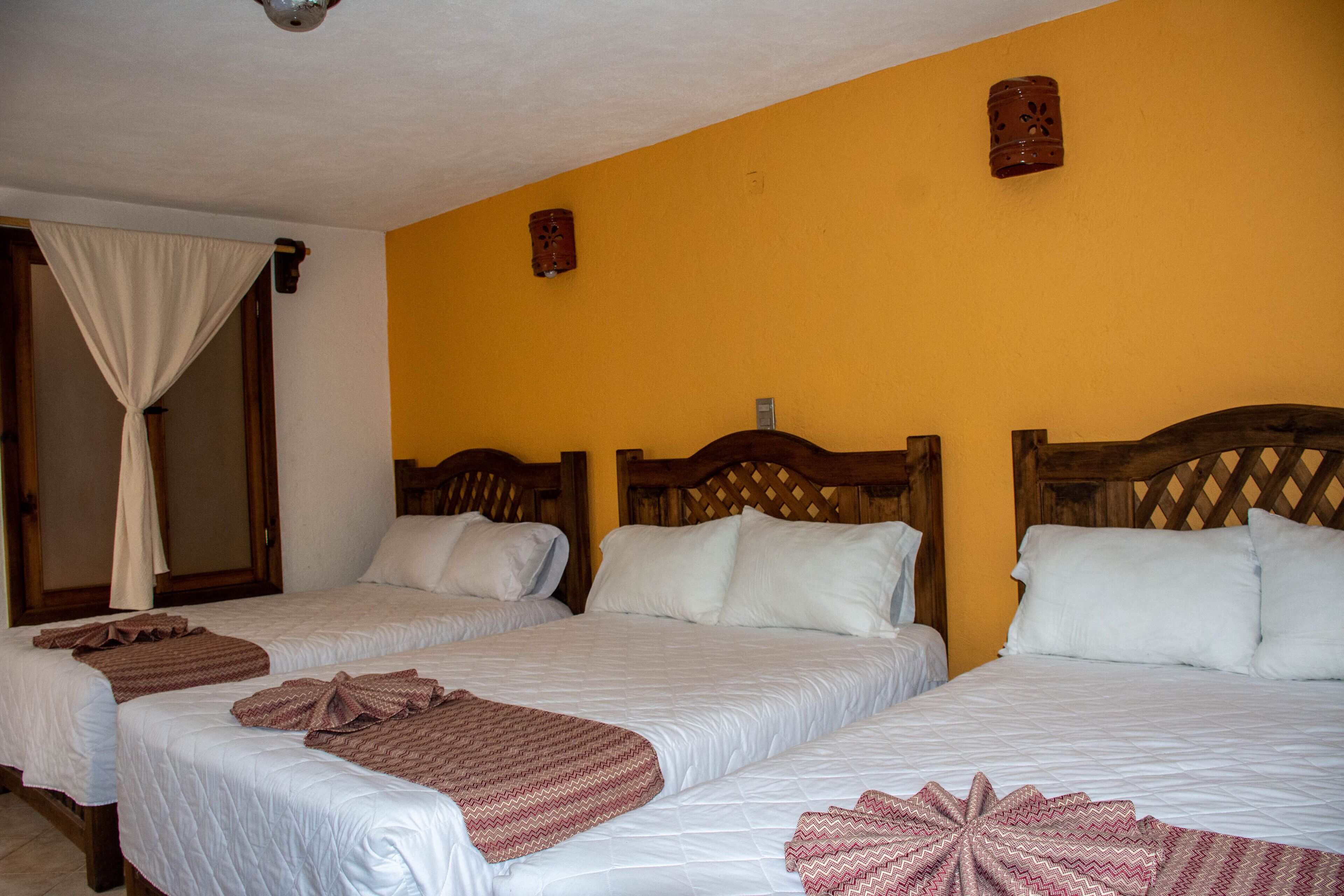 Habitación de hotel con dos camas, cabeceros de madera y una pared amarilla.