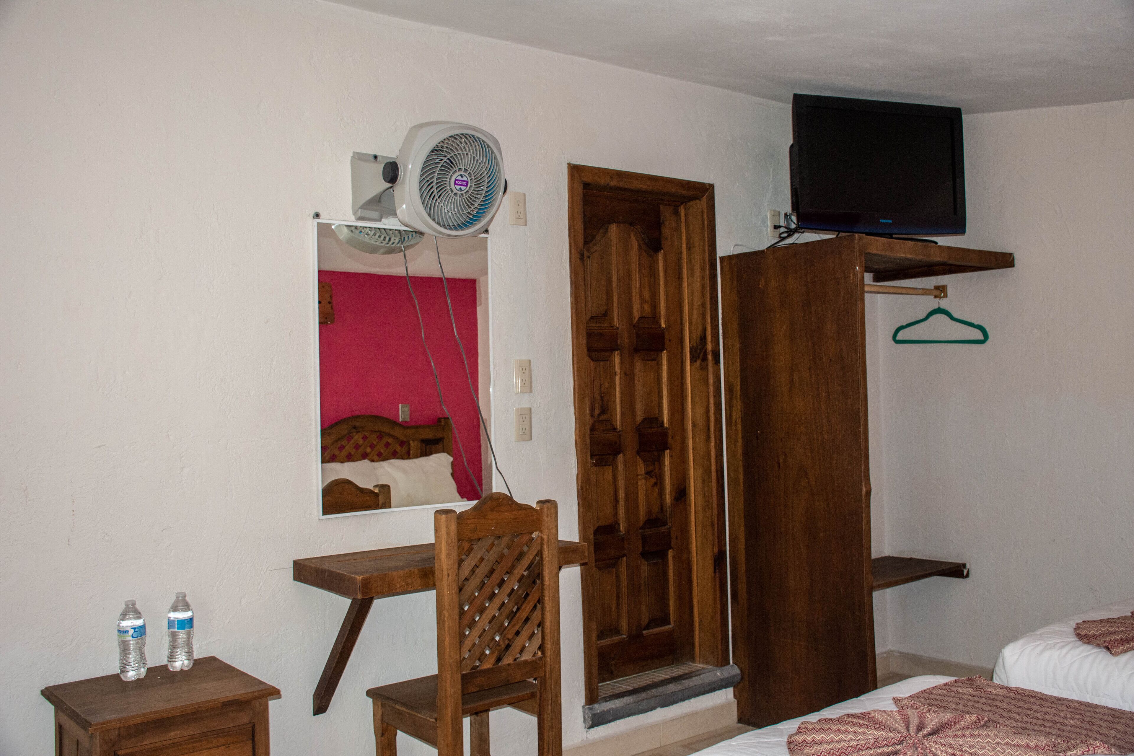 A room with a wooden desk, a chair, a bed, a television, and a mirror.