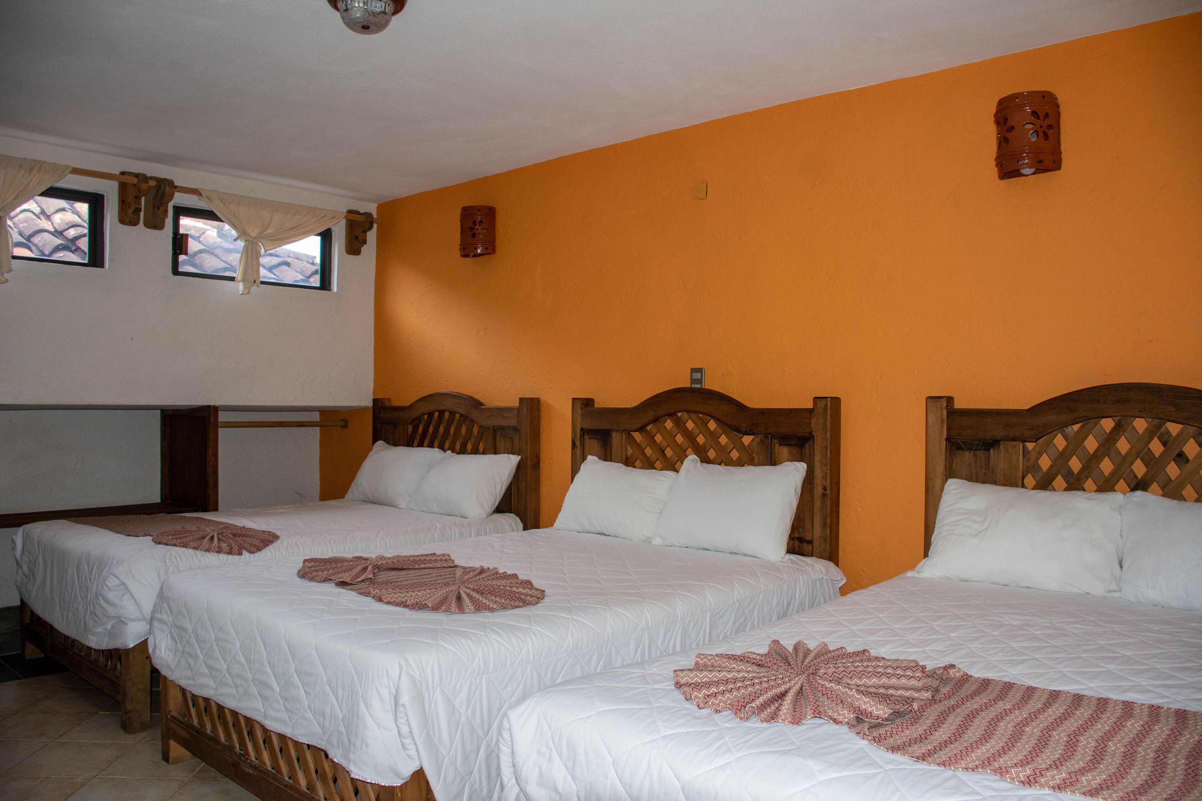 Habitación de hotel con dos camas, cabeceros de madera y una pared de color naranja brillante.