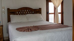 A bedroom with a wooden bed frame, white bedding, and a window with curtains. - Hotel Real del Carmen (San Cristóbal de las Casas)