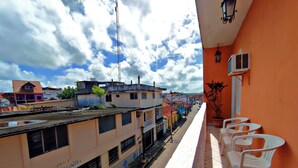 A balcony with white plastic chairs, a tiled floor, and a view of a train station with tracks and buildings in the background. - Hotel Posada de la Jungla (Flores)