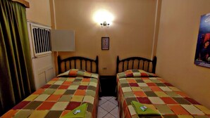 A room with two single beds, a window with blinds, a wall-mounted light, and a framed picture. - Hotel Posada de la Jungla (Flores)