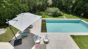A poolside area with a tiled deck, two lounge chairs, a table with a pink tray, and a white umbrella. - Hossegor Proche Lac, Villa 8 Personnes, Piscine (HOSSEGOR)