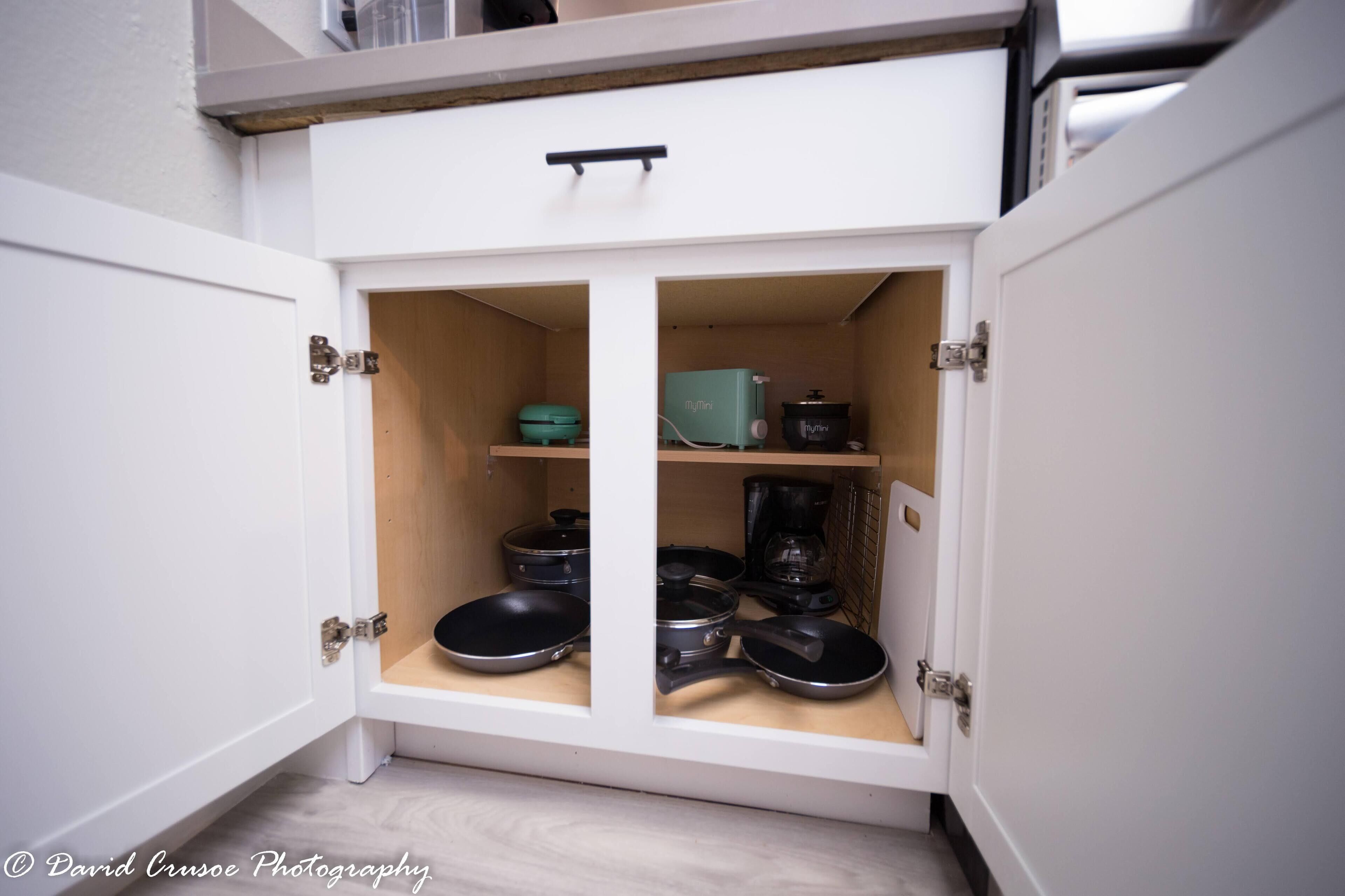 A white cabinet with two open doors, containing kitchenware like pans and a coffee maker.