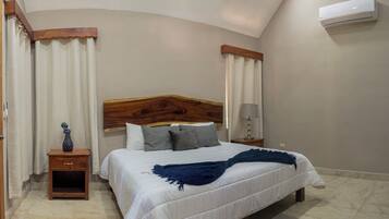 Un dormitorio con cabecera de madera, una mesita de noche con lámpara, un jarrón y una cama con una manta azul.