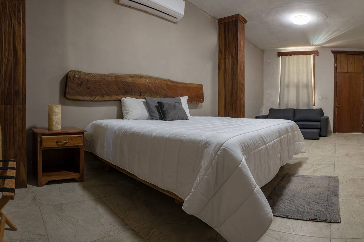 Une chambre à coucher avec un grand lit, une table de chevet, une tête de lit en bois, un canapé gris et une armoire en bois.