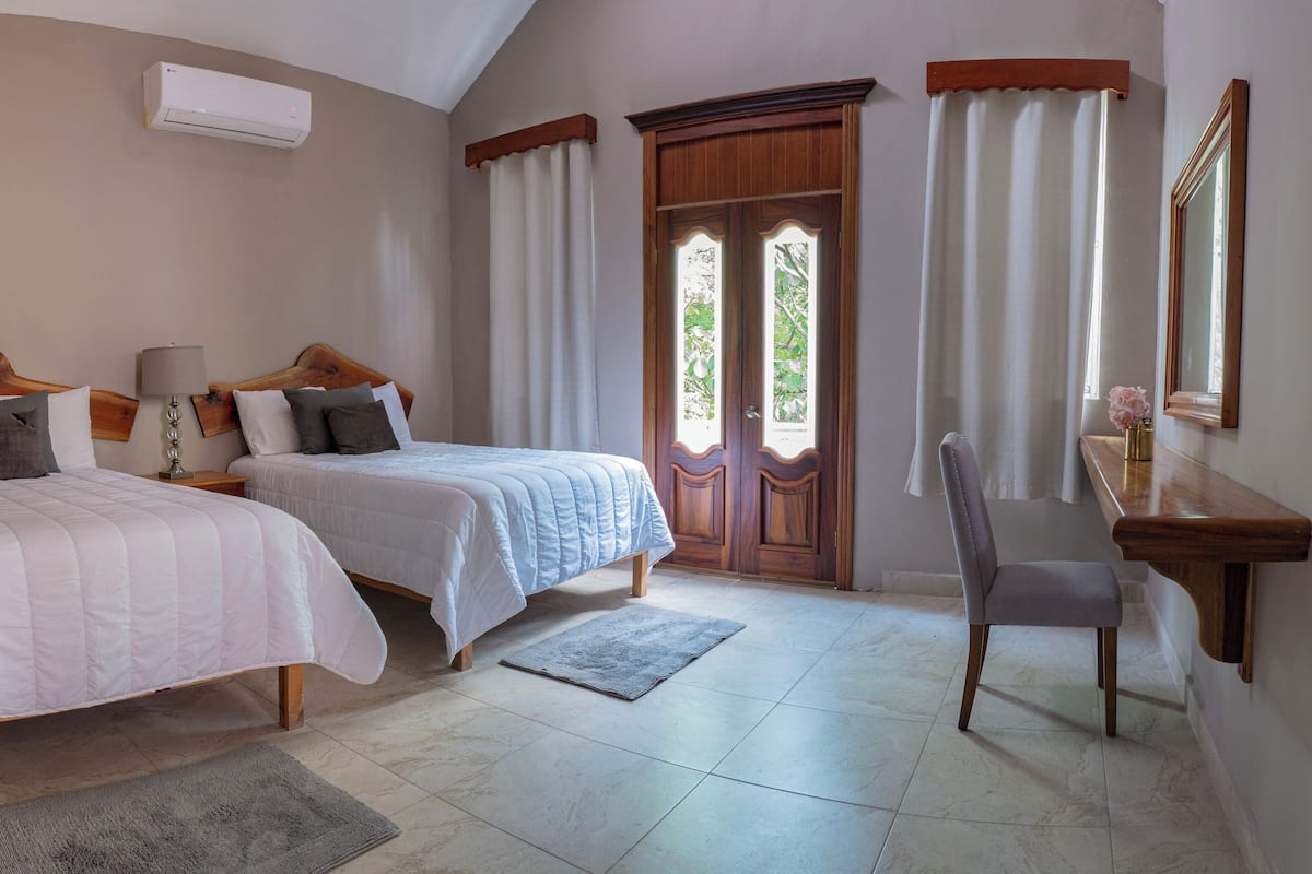 Une chambre avec deux lits, un bureau, une chaise et une fenêtre avec des rideaux.