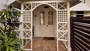 A house with a white porch, a wooden fence, and a door with a 'Friends Welcome' mat. - Cosy cottage near the beautiful West Coast beaches (Holetown)