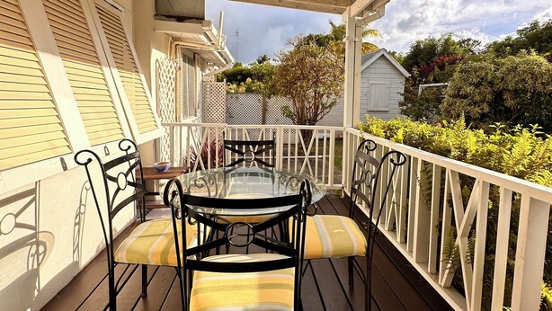 A covered outdoor patio with a table and chairs, a ceiling fan, and a view of the surrounding landscape. - Cosy cottage near the beautiful West Coast beaches (Holetown)