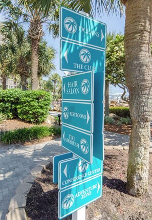 A directional sign with arrows pointing to various hotel amenities including the club, hair salon, restrooms, tiki airbrush, conference center, and adventure zone.