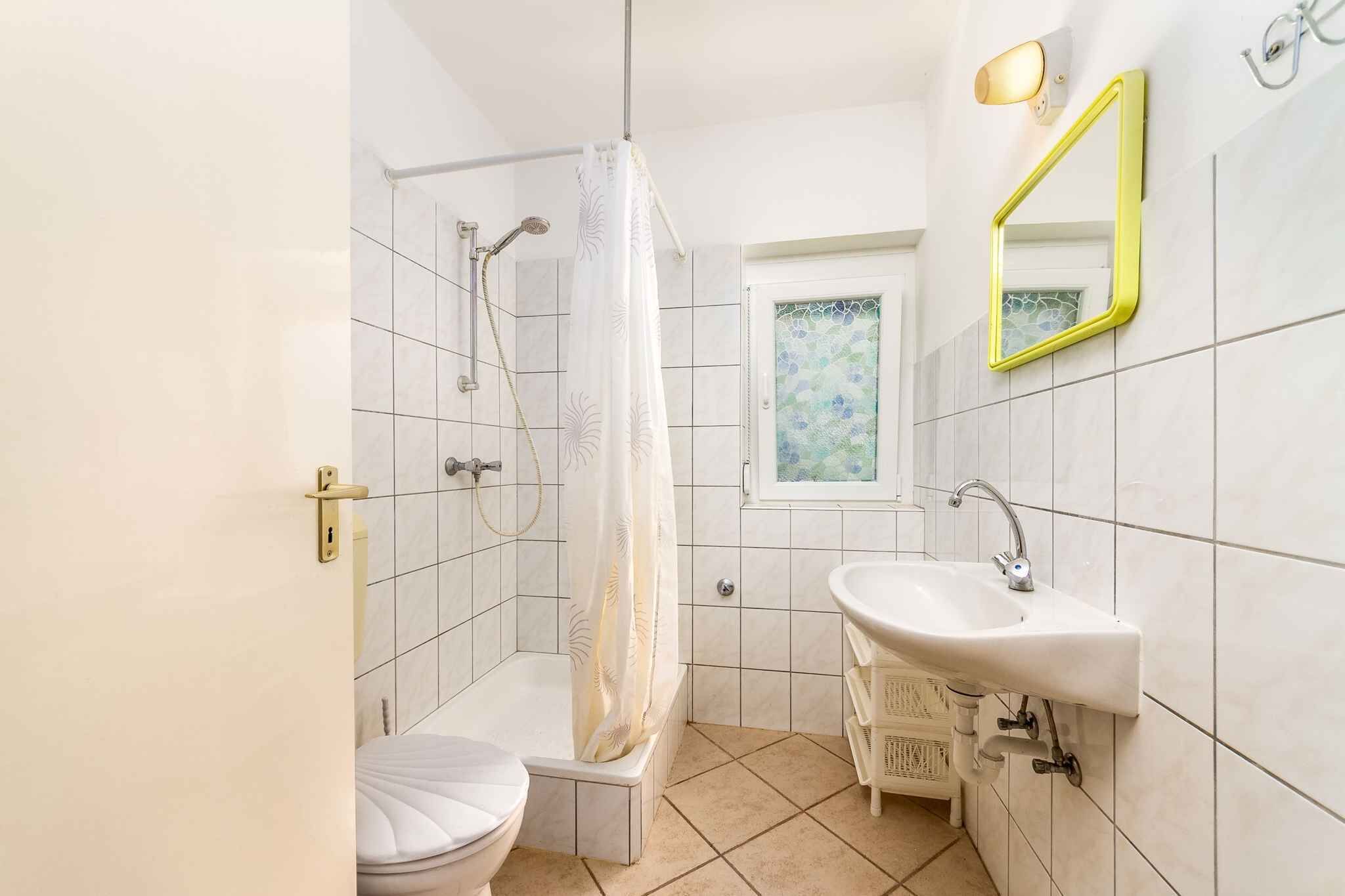 Badeværelse med brusebad, toilet, håndvask og et vindue med dekorativt glas.