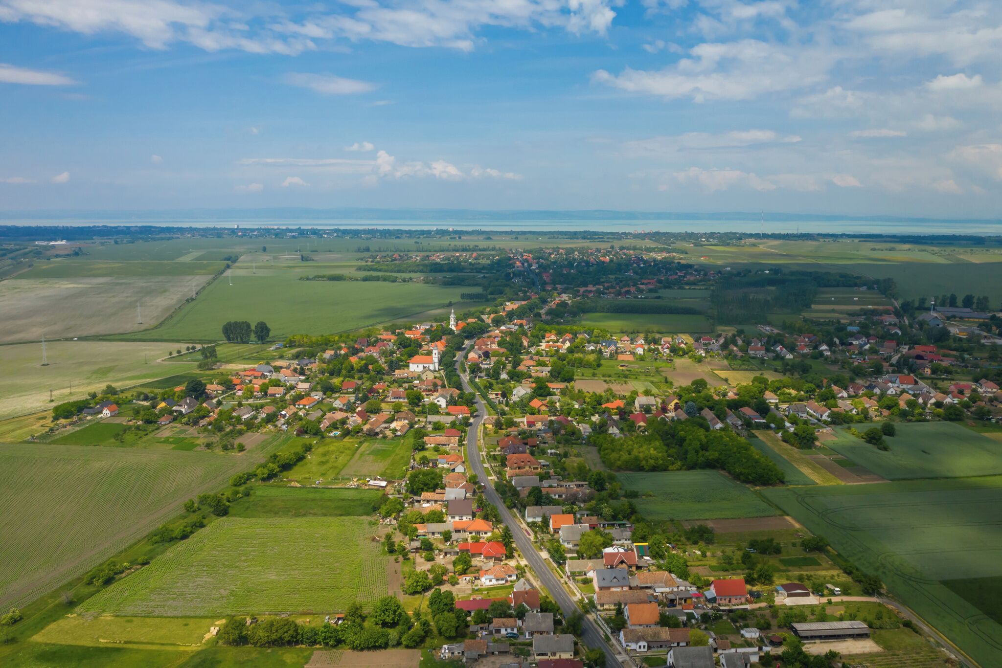 Eine Vogelperspektive einer kleinen Stadt mit einer zentralen Straße, grünen Feldern und Wohngebäuden.