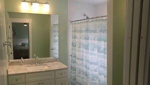 A bathroom with a vanity, a mirror, a shower curtain with a bird pattern, and a light fixture above the mirror. - 19988 Front Beach Rd (Panama City Beach)