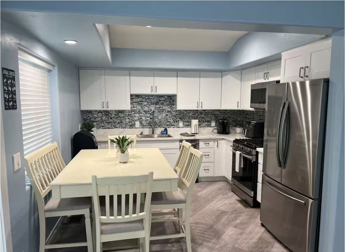 A modern kitchen with white cabinets, a stainless steel refrigerator, and a dining table with chairs.