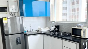 A modern kitchen with white cabinets, a stainless steel refrigerator, a microwave, and a gas stove.