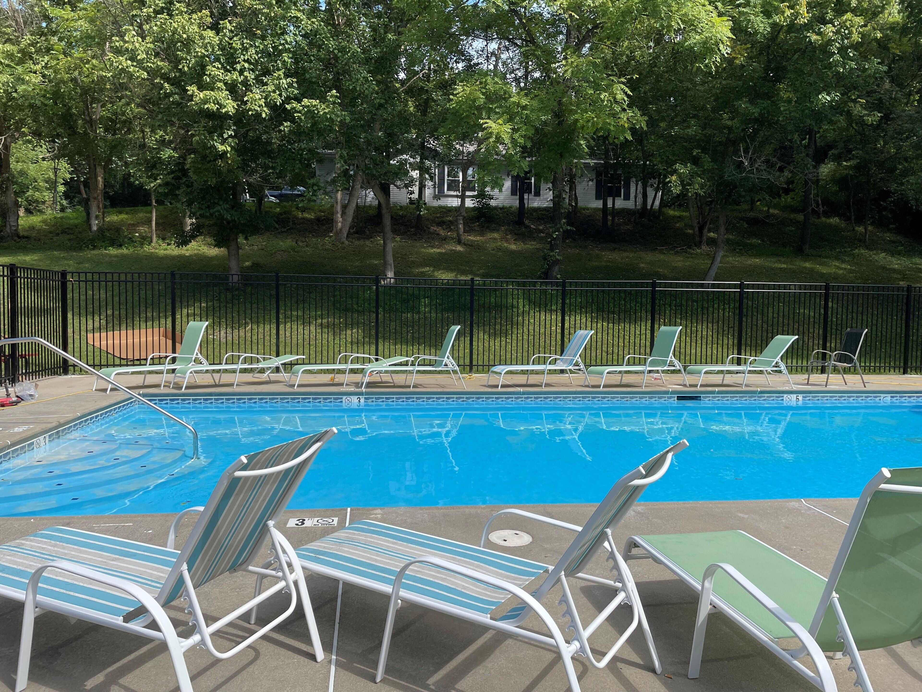 A swimming pool with lounge chairs and a fence.