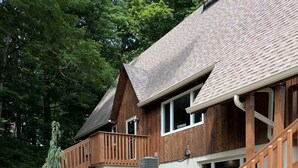Une maison en bois à deux étages, dotée d’un balcon, d’un chemin en pierre et de petits arbustes.
