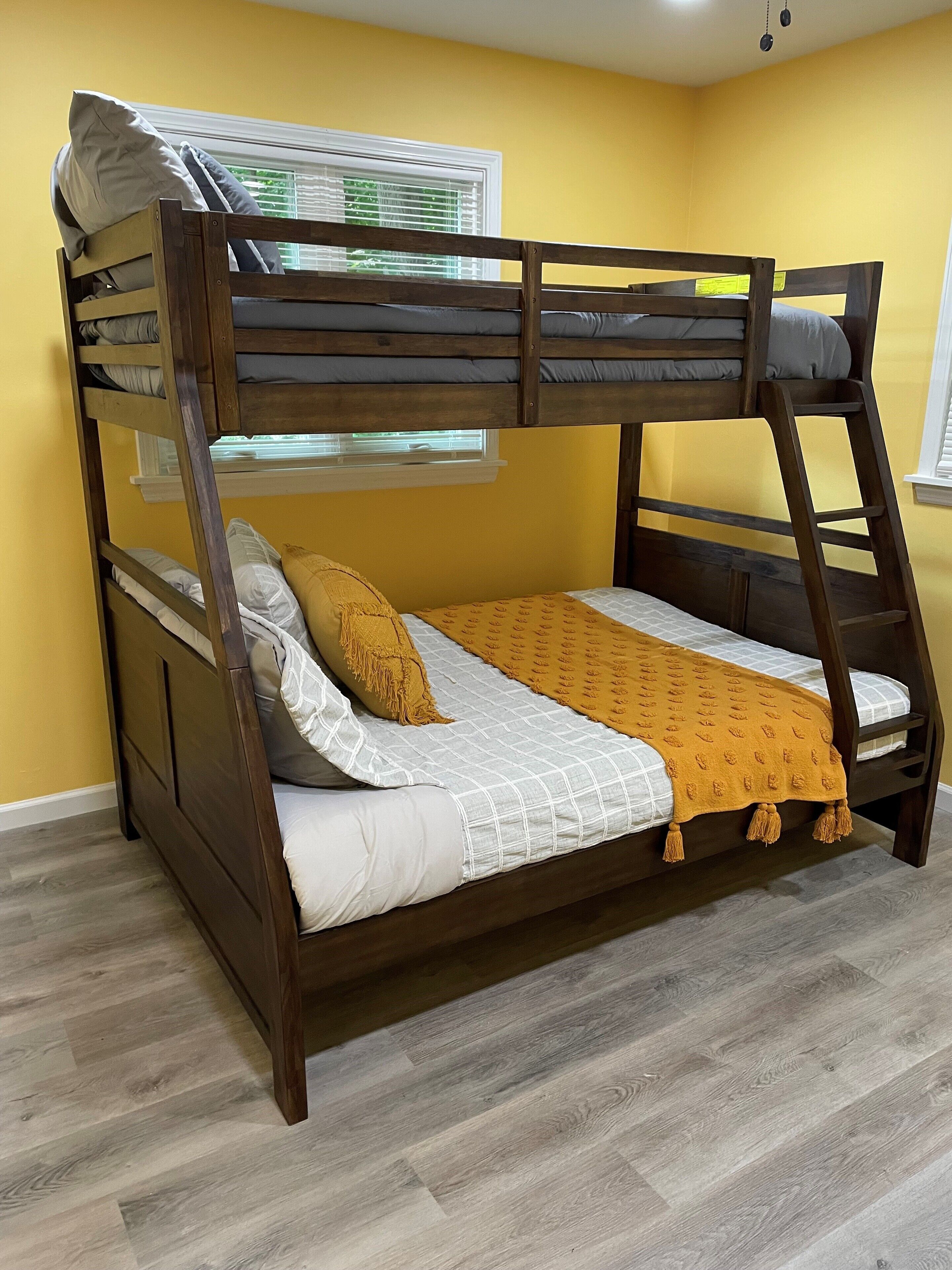 A bunk bed with a wooden frame, white bedding, and a mustard-colored throw blanket.