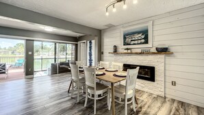 A dining area with a wooden table and white chairs, a fireplace, and a large window overlooking a deck. - Relaxing Vacation Home on Water Next To Siesta Key (Sarasota)