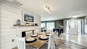 A dining area with a wooden table set for six, white chairs, and a fireplace with a painting above it. - Relaxing Vacation Home on Water Next To Siesta Key (Sarasota)