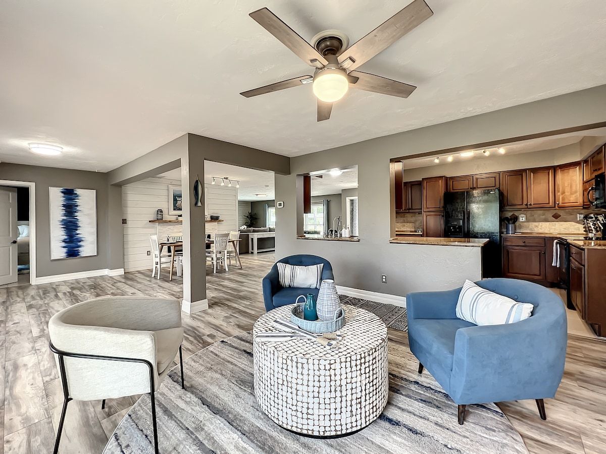 Un salon moderne doté d’un ventilateur de plafond, d’une table basse ronde, d’un canapé bleu et d’un coin repas avec une table et des chaises blanches.
