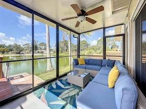 A sunlit room with a large window, a ceiling fan, a sectional sofa, and a patterned rug. - Relaxing Vacation Home on Water (Sarasota)