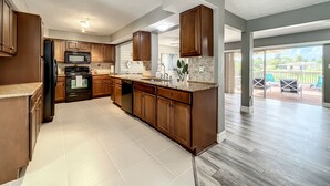 A modern kitchen with wooden cabinets, a black refrigerator, and a large island. - Relaxing Vacation Home on Water Next To Siesta Key (Sarasota)
