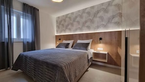 A modern bedroom with a large bed, a nightstand, a wall-mounted lamp, and a patterned wallpaper. - Holiday apartment with swimming pool and sea view (Šilo)